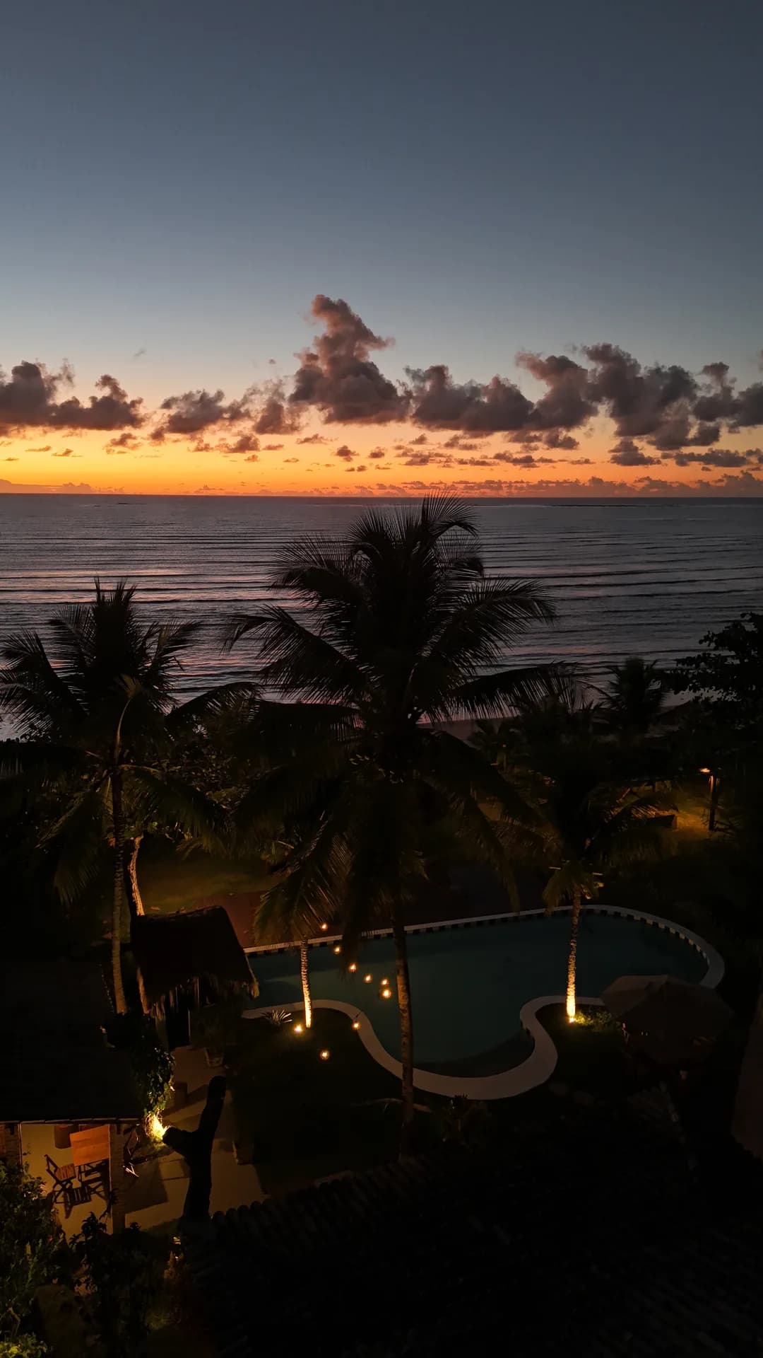 Céu alaranjado sobre o mar e a piscina iluminada da Mayon